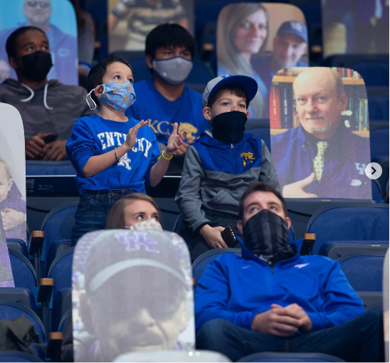 These fans in December 2020 enjoy a Kentucky Wildcats men’s basketball game, even though the threat of the COVID-19 pandemic causes fans to wear a mask and sit next to cardboard cutouts.