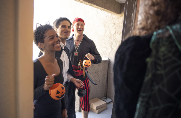 Three adults are arriving at a house to take part in the forever-lasting tradition established during Halloween–Trick or Treat.