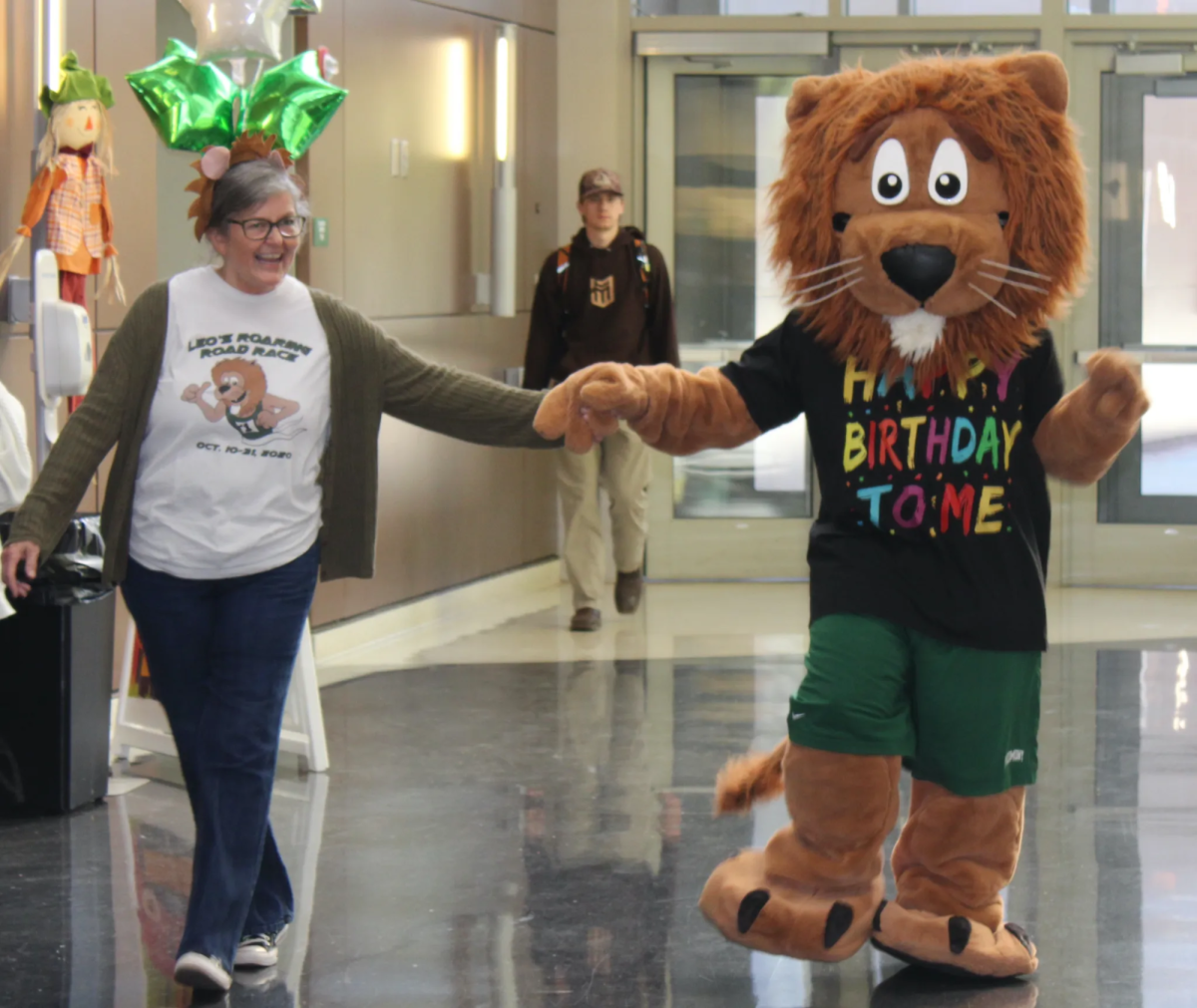 Leo the Lion locks hands with staff member Terrie Ellerbee as he makes his way to his 128th birthday celebration, ready for a day full of fun and festivities.